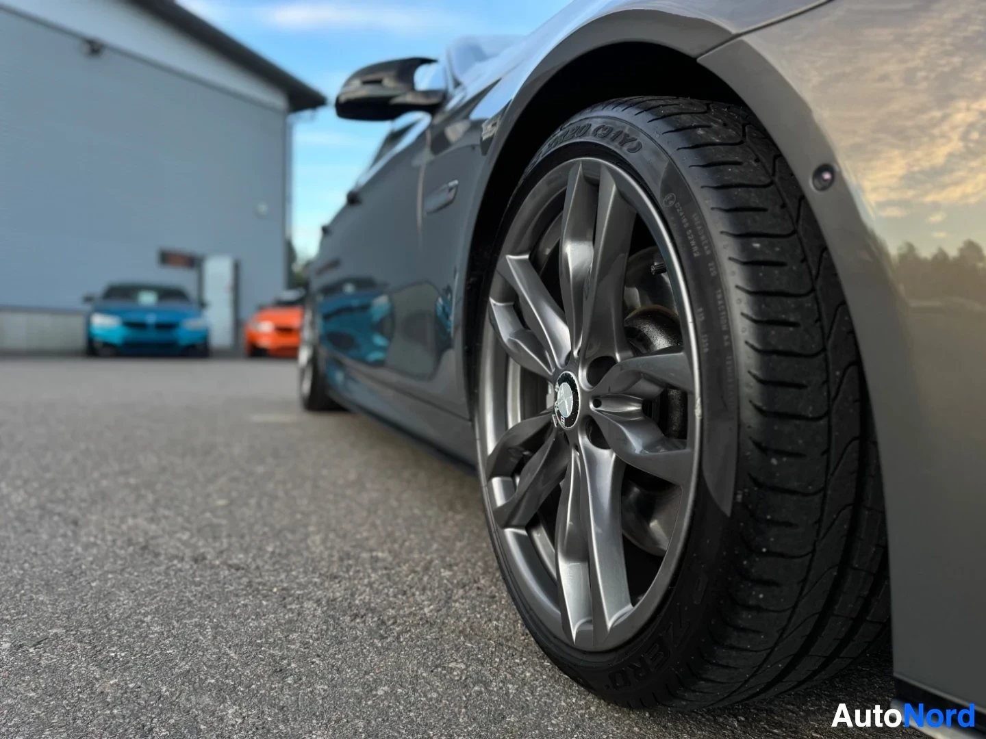 Yksityiskohta: Auton etupyörän ja sivupaneelin alaosan lähikuva, kuvattu matalasta kulmasta. Kymmenpuolaisissa vanteissa on BMW-logo, ja renkaan sivussa näkyy teksti 'P Zero'.