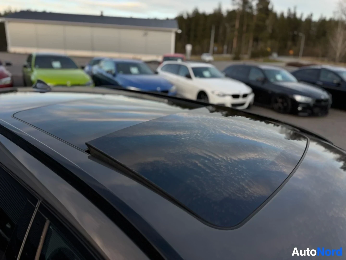 Yksityiskohta: Lähikuva auton katolla olevasta lasisesta kattoluukusta, josta heijastuu pilvinen taivas. Auton edessä ja takana näkyy muita autoja.