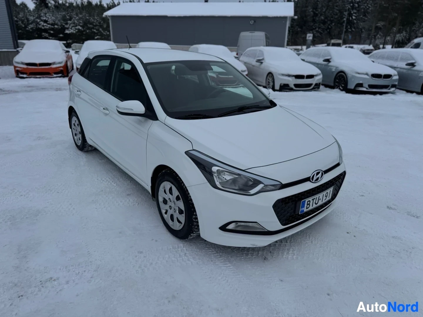 Etuviisto, nokka vasemmalle: Valkoinen henkilöauto pysäköitynä lumiselle piha-alueelle. Rekisterikilpi "" näkyy auton edessä