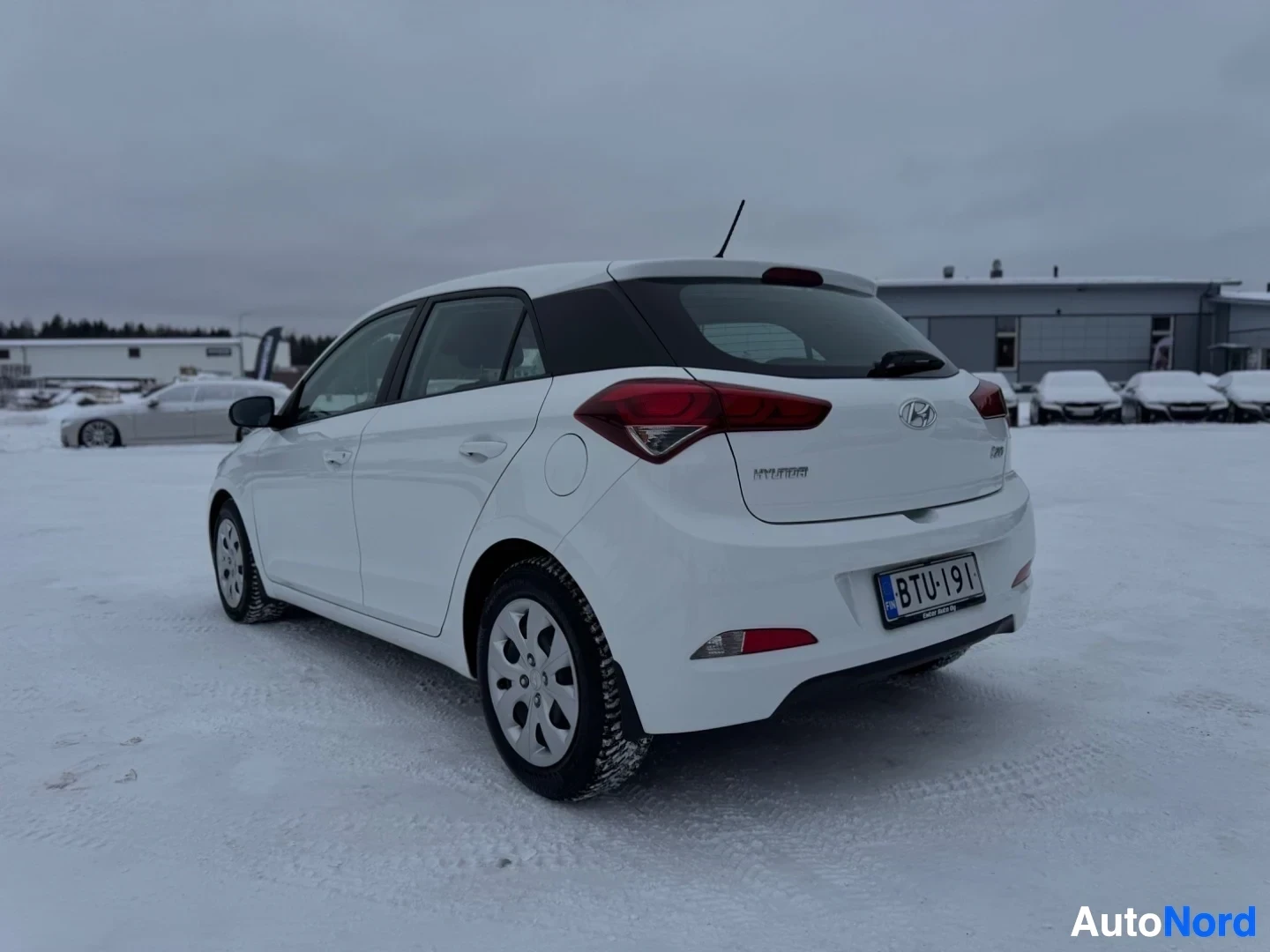 Takaviisto: Valkoinen henkilöauto takaviistosta kuvattuna lumisella parkkipaikalla. Takaluukussa lukee "Hyundai" ja rekisterikilpi "" näkyy