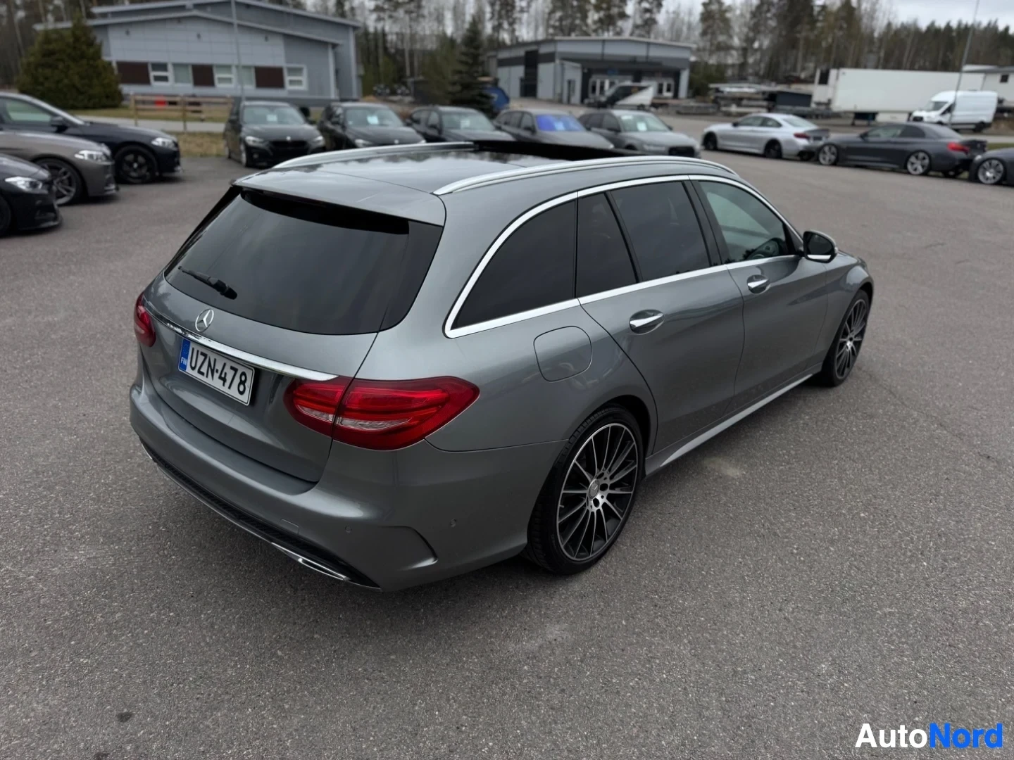 Takaviisto: Harmaa farmariauto takaoikealta ylhäältä kuvattuna, rekisterikilvessä teksti ""