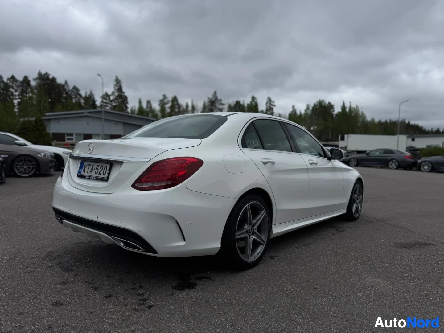 Takaviisto: Valkoinen sedan-auto pysäköitynä ulos, takaosa ja oikea kylki näkyvissä.