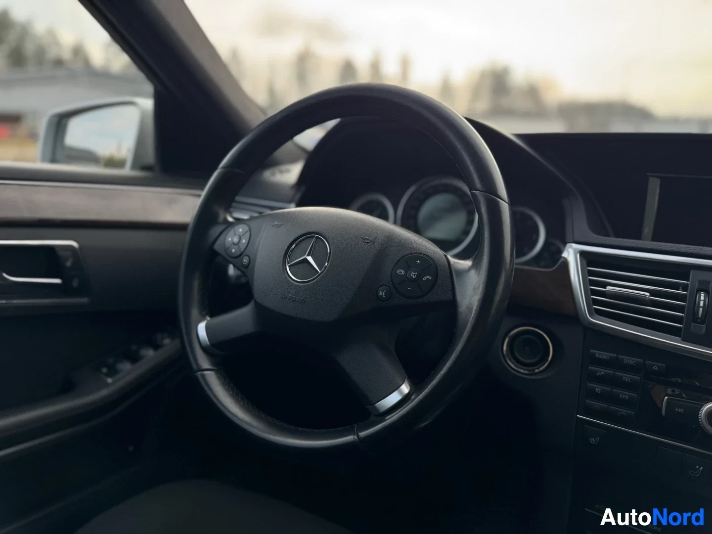 Yksityiskohta: Lähikuva auton ohjauspyörästä ja osasta kojelautaa. Ohjauspyörässä on Mercedes-Benzin logo ja painikkeet.