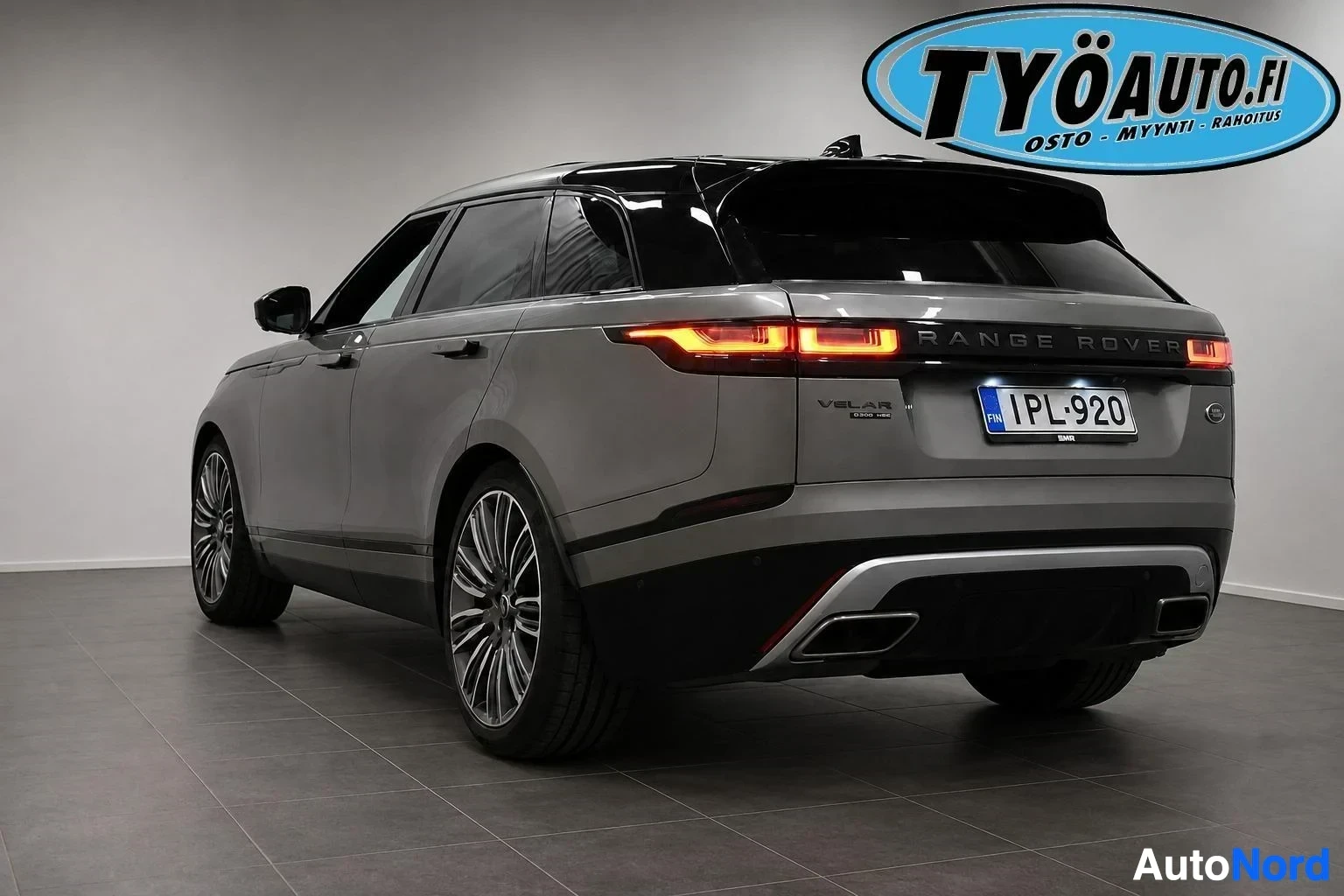 Takaviisto: Harmaa Range Rover Velar takaa ja vasemmalta sivulta kuvattuna autohallissa. Autossa on musta katto, takaspoileri, tummennetut takalasit ja mustat monipuolaiset