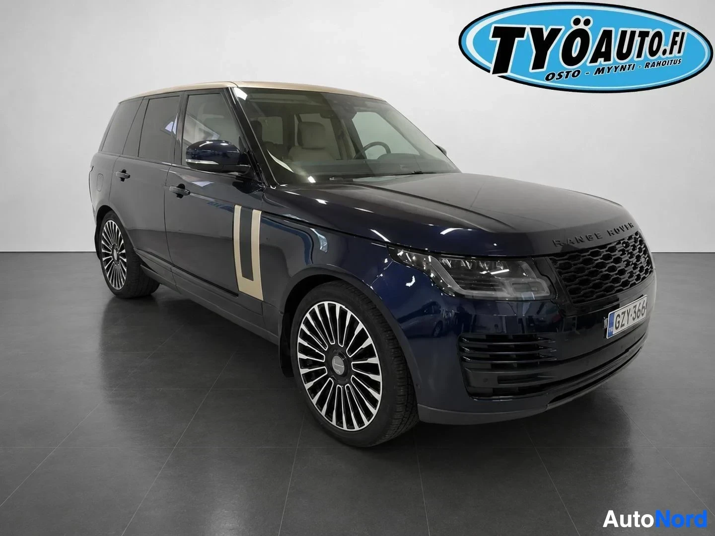 Etuviisto, nokka oikealle: Tummanvärinen Range Rover -SUV edestä ja oikealta sivulta. Siinä on beigen värinen katto ja koristeteipit ovissa. Rekisterikilpi "" näkyy