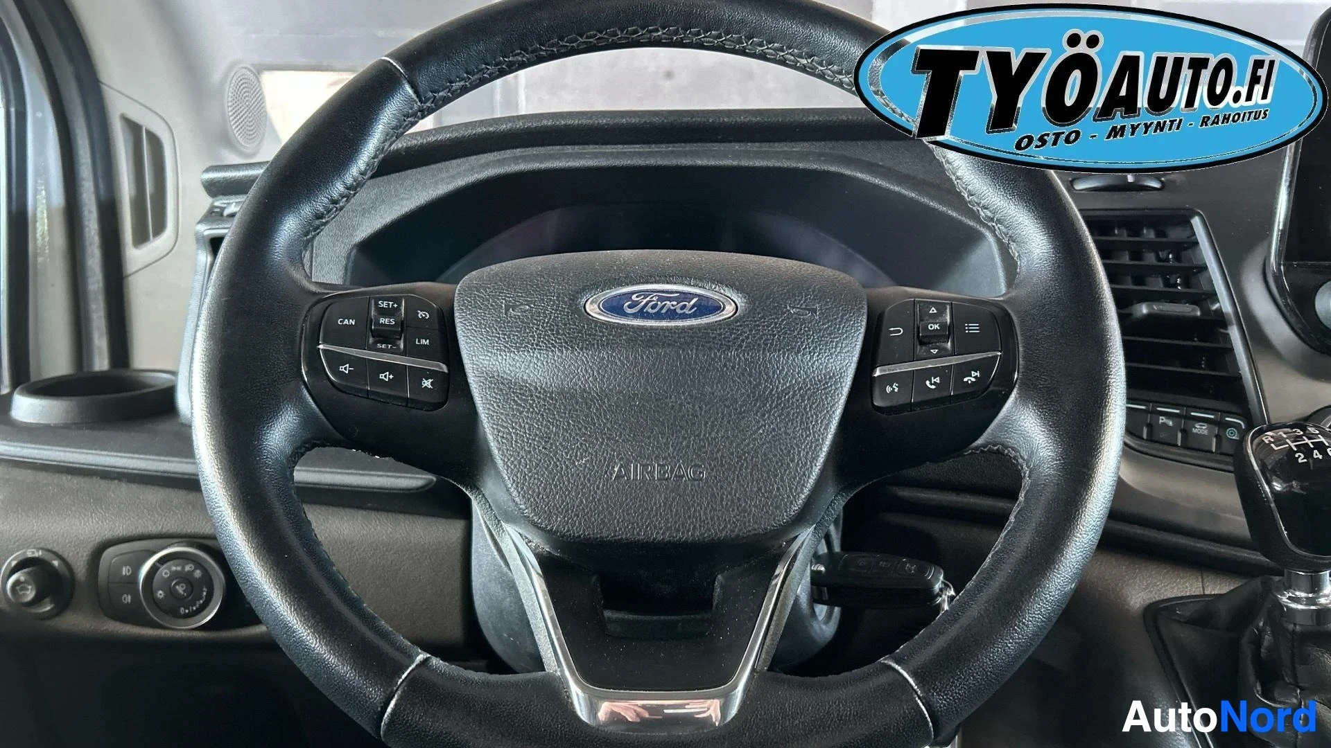Yksityiskohta: Lähikuva ohjauspyörästä, jossa näkyy Ford-logo, "AIRBAG"-teksti ja monitoiminäppäimet vasemmalla (SET+, RES, CAN, SET-, nuoli ylös, nuoli alas, nuoli vasemmalle