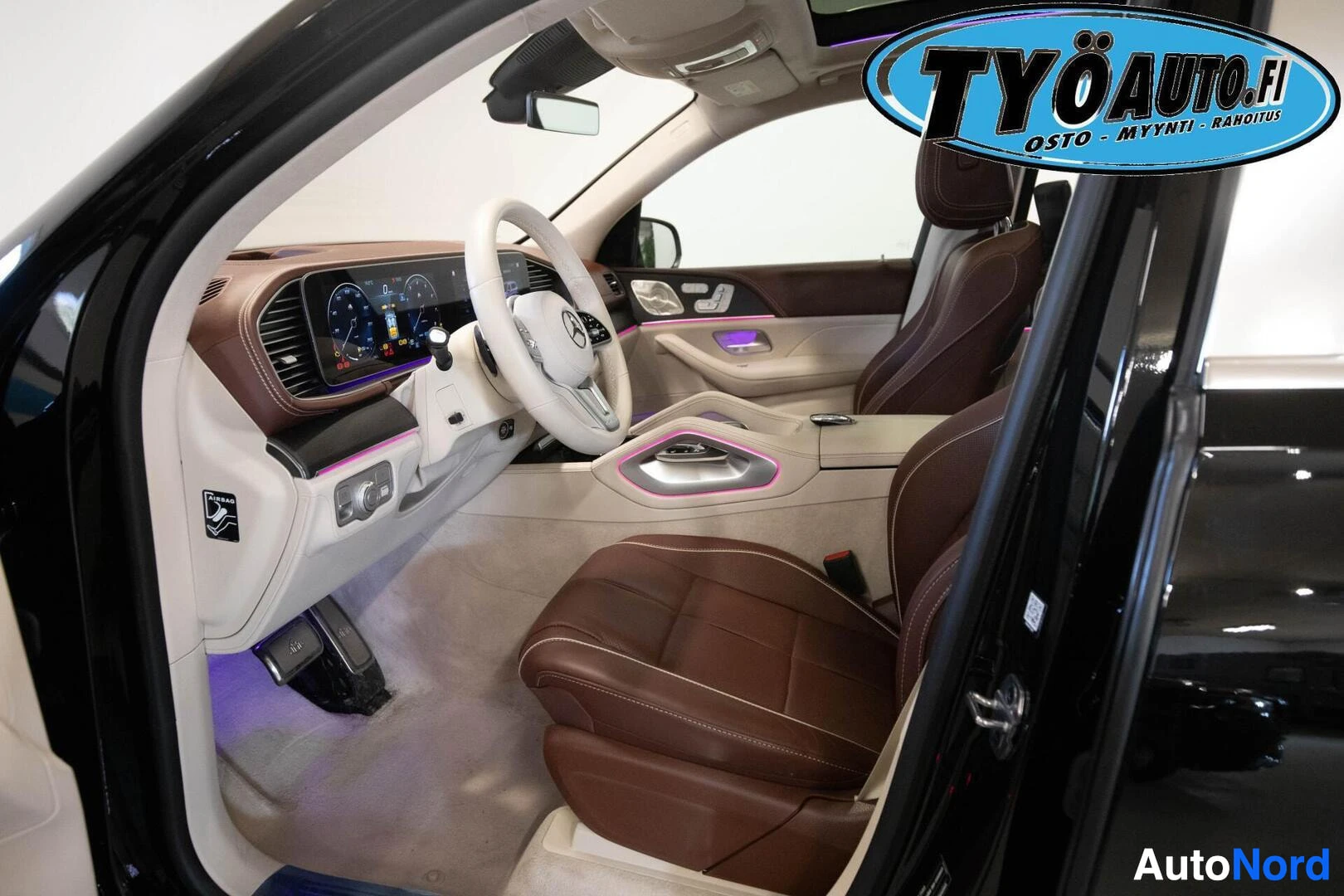Ohjaamo: Auton sisätilat vasemmasta etuovesta kuvattuna. Ruskeat nahkaistuimet edessä ja vaalea kojelauta. Autossa on valkoinen ohjauspyörä.