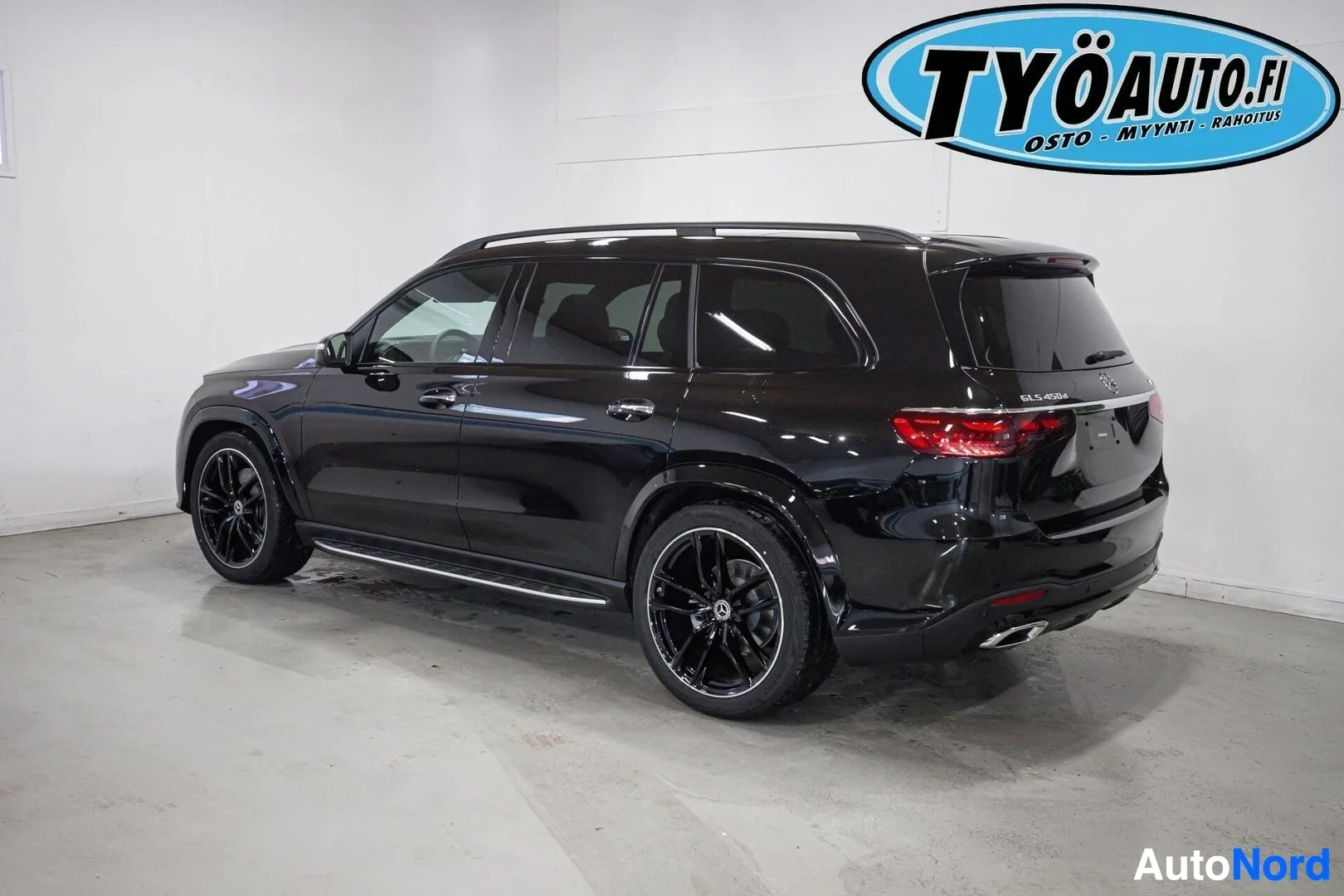 Takaviisto: Musta Mercedes-Benz SUV takaa vasemmalta kuvattuna sisätiloissa. Takaluukun oikealla puolella on mallimerkintä GLS 450 d 4MATIC. Autossa on mustat monipuolaiset