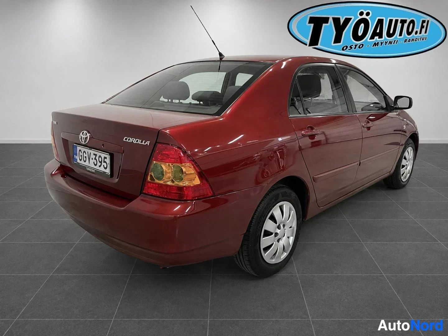 Takaviisto: Punainen Toyota Corolla -henkilöauto pysäköitynä taka-oikealta viistosta kuvattuna. Auton takaosa ja oikea kylki näkyvät. Rekisterikilpi "" on näkyvissä
