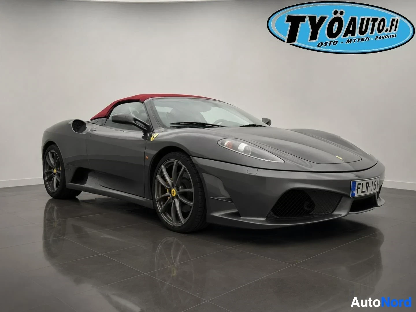 Etuviisto, nokka vasemmalle: Harmaa Ferrari F430 Spider -urheiluauto edestä oikealta, pehmeä katto ylhäällä, rekisterikilpi