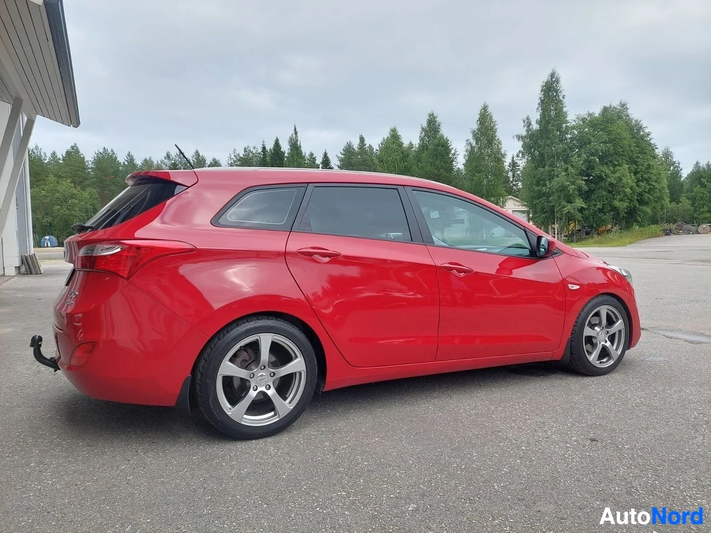 Sivulta: Punainen henkilöauto sivulta päin. Autossa on viisipuolaiset kevytmetallivanteet ja katolla kattokiskot.