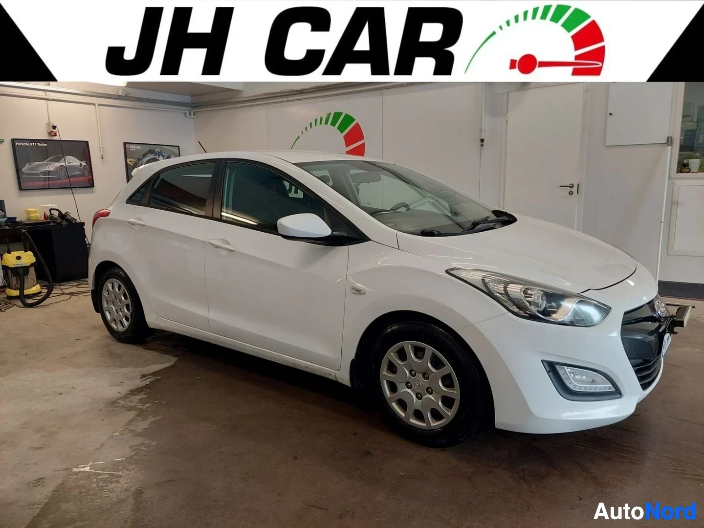 Etuviisto, nokka oikealle: Valkoinen Hyundai i30, jossa on metalliset vanteet. Auton keula ja vasen kylki näkyvät etuviistosta.