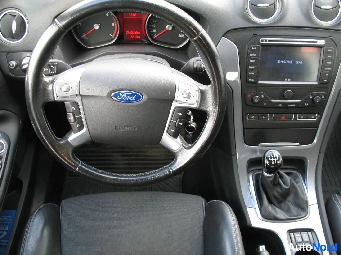 Ohjaamo: Kojelaudan ja ohjauspyörän lähikuva. Ohjauspyörässä on monitoimipainikkeet ja Ford-logo, ja mittaristossa näkyy lukema 246593 km.