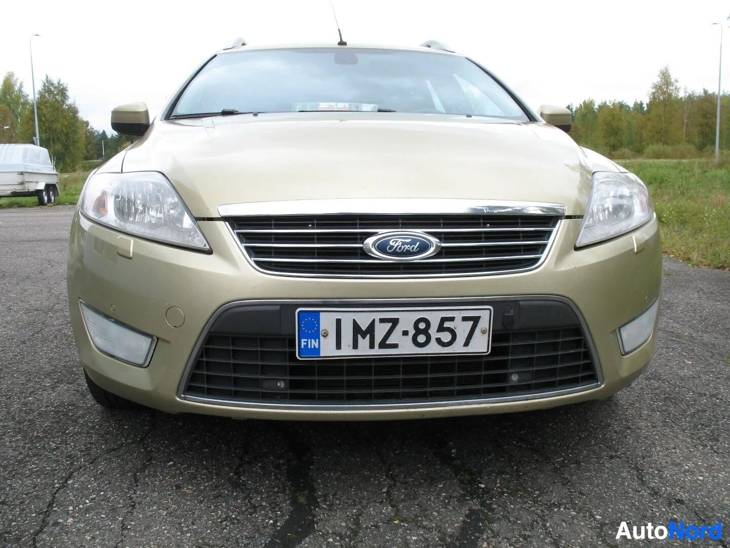Edestä: Ford Mondeo farmariauton etuosa edestäpäin kuvattuna, ajovalot päällä. Autossa on Ford-logo ja rekisterikilpi "FIN "