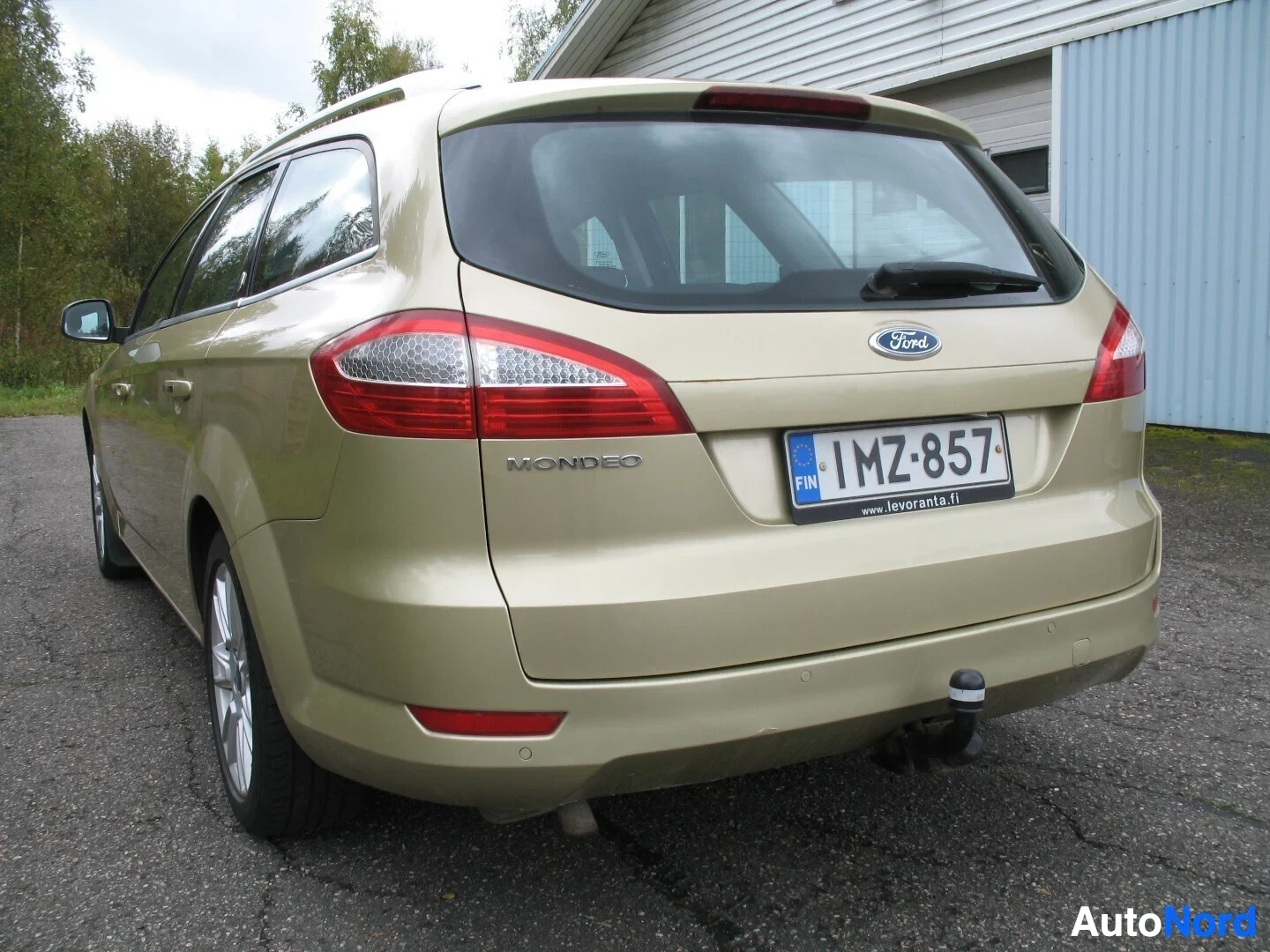 Takaviisto: Kultaisen farmariauton takaosa, jossa näkyy peräkontin luukku, takavalot, Ford-logo, rekisterikilpi "", vetokoukku ja takapuskuri. Rekisterikilven alla l