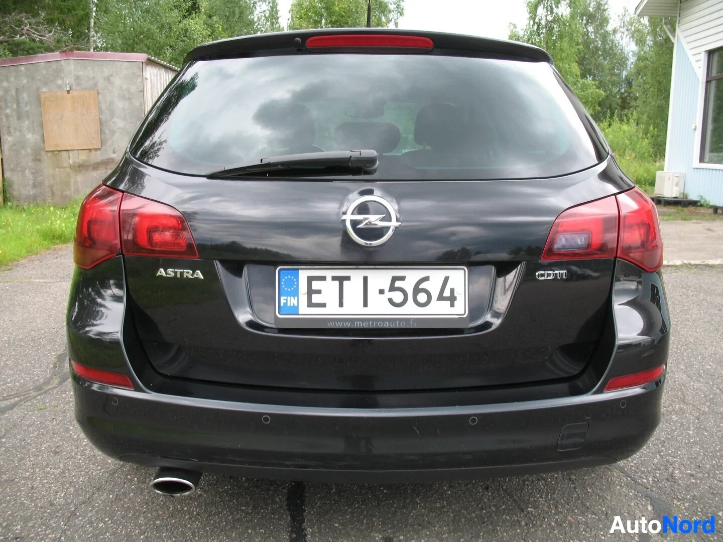 Takaa: Musta farmariauto takaa kuvattuna. Takaosassa näkyy takavalot, takaluukku, takalasinpyyhin, Opel-logo, rekisterikilpi "", "ASTRA"-merkki vasemmalla ja "C
