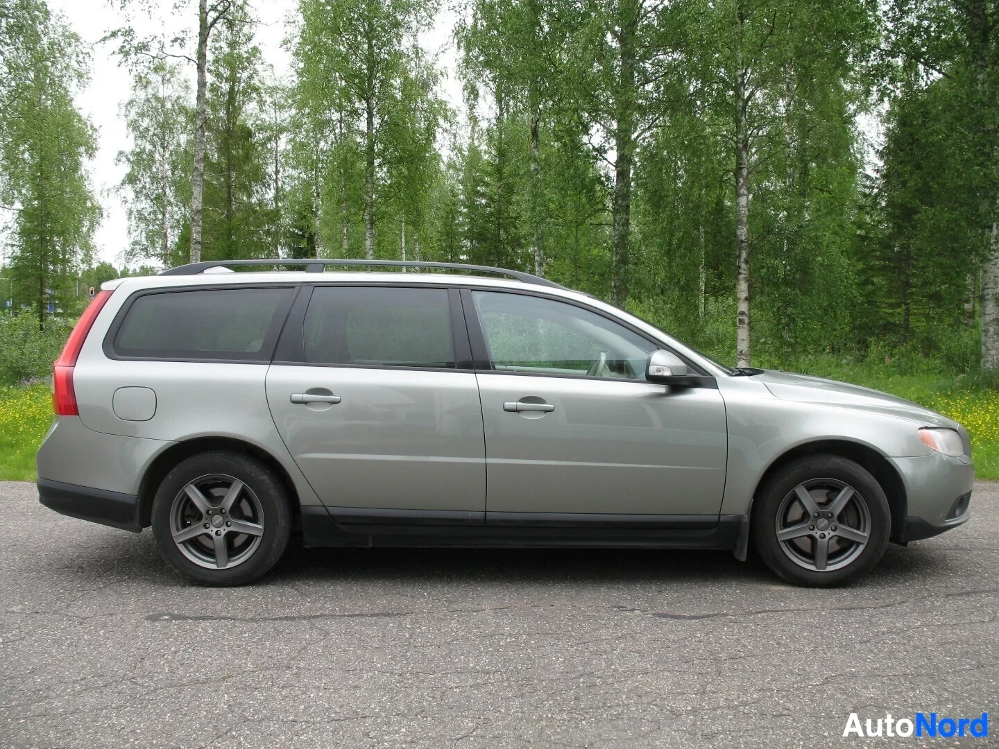 Sivulta: Harmaa farmariauto sivulta päin. Katolla kattokaiteet ja renkaissa kevytmetallivanteet.