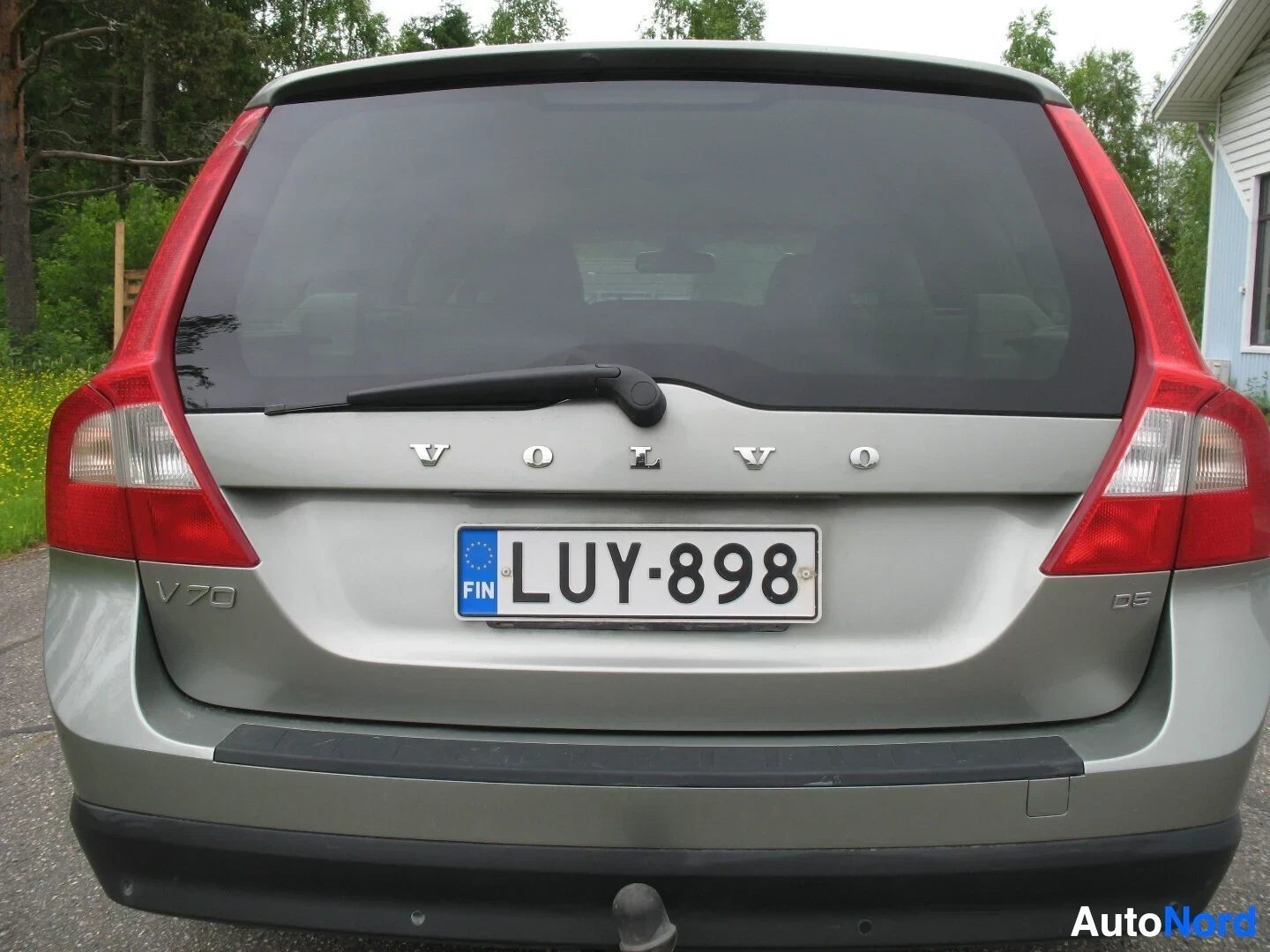 Takaa: Harmaan farmariauton takaosa, jossa rekisterikilpi "", VOLVO-merkki ja V70- ja D5-mallimerkinnät. Takapuskurin alaosassa vetokoukku