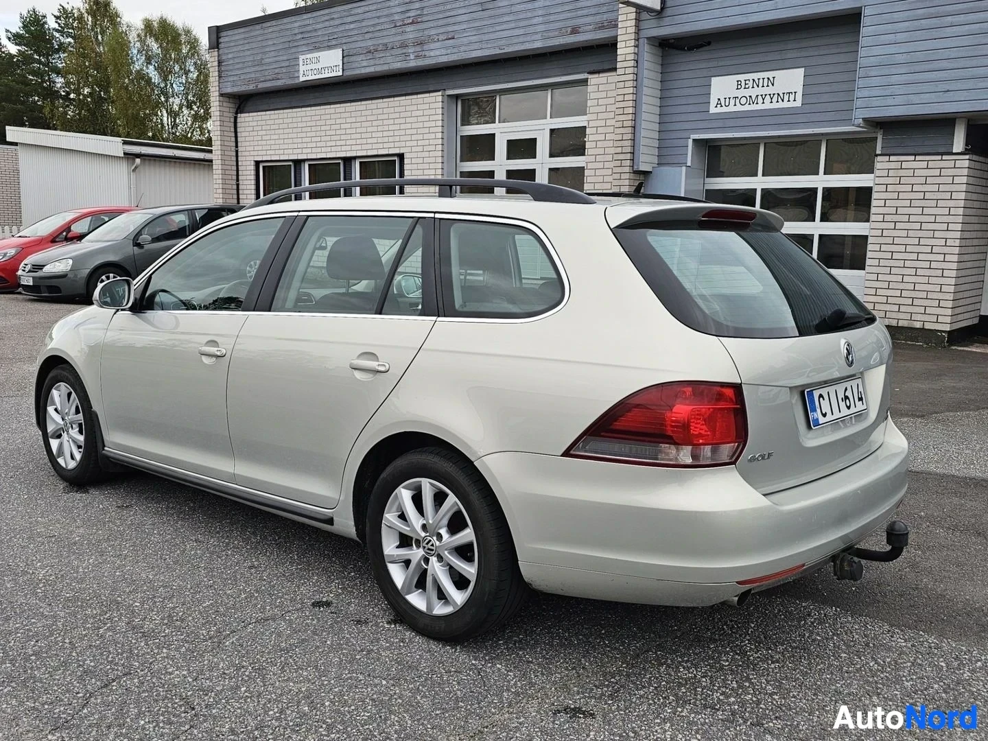 Takaviisto: Hopeanvärinen Volkswagen Golf Variant, jossa on kattokaiteet, alumiinivanteet ja vetokoukku, pysäköitynä rakennuksen eteen. Auton takaosa ja vasen kylki ovat nä