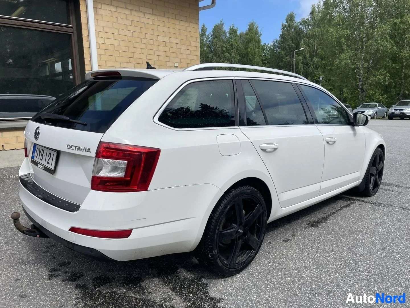 Takaviisto: Auton takaosa ja oikea kylki kuvattuna viistosti takaoikealta. Autossa on valkoiset kattokiskot, tummat takalasit ja vetokoukku. Rekisterikilpi "" on näkyvissä.