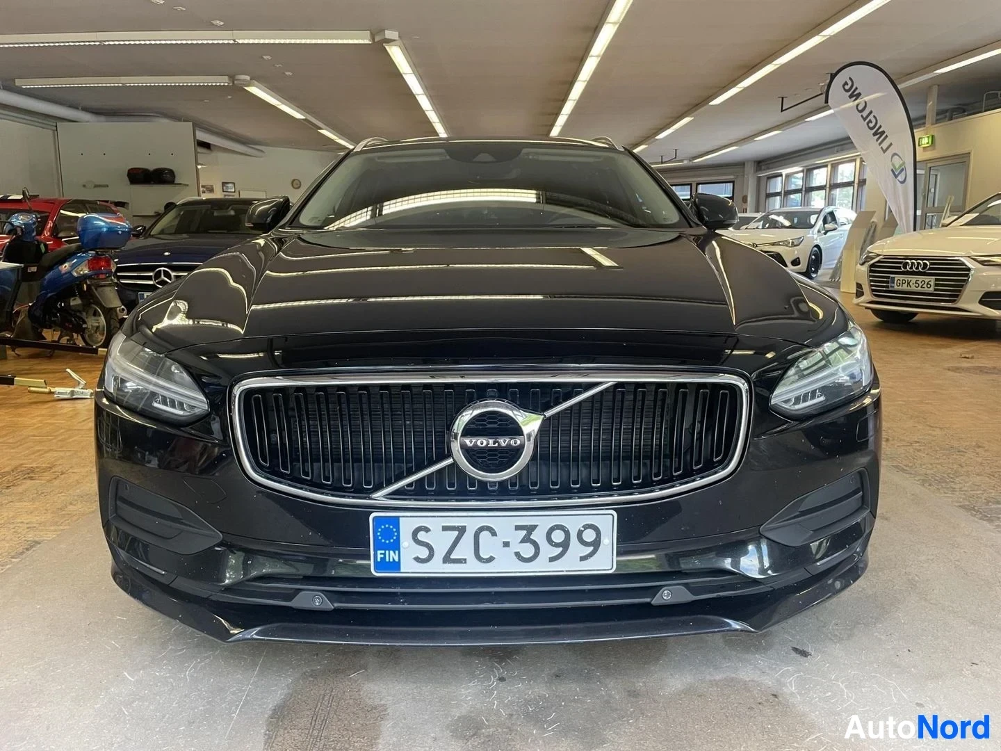 Edestä: Musta Volvo V90, jossa on keulan suoraan edestäpäin otettu kuva. Rekisterikilvessä on teksti "".