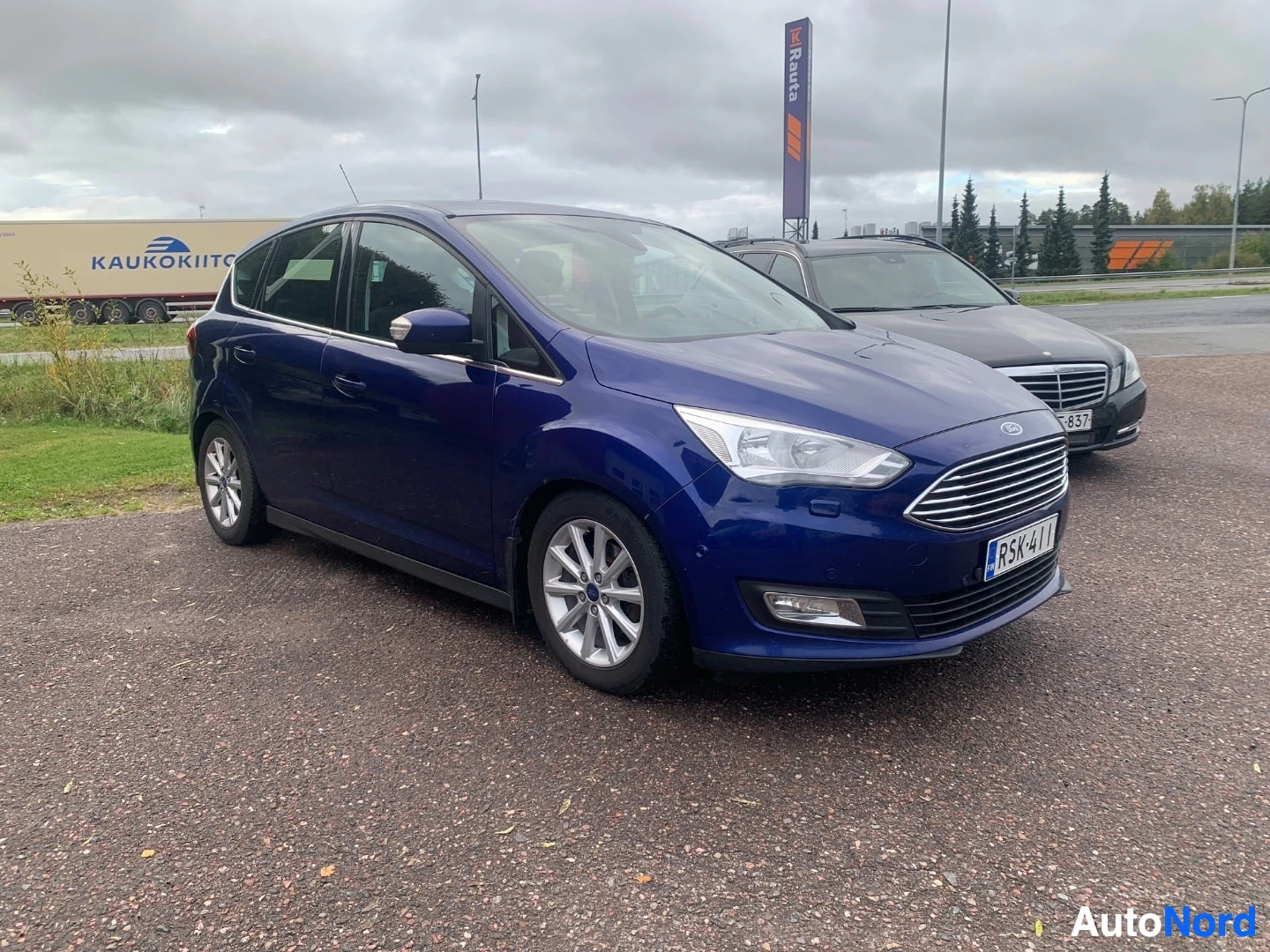 Etuviisto, nokka oikealle: Sininen tila-auto kolmesta neljäsosasta edestä oikealta kuvattuna, keula ja vasen kylki näkyvissä.