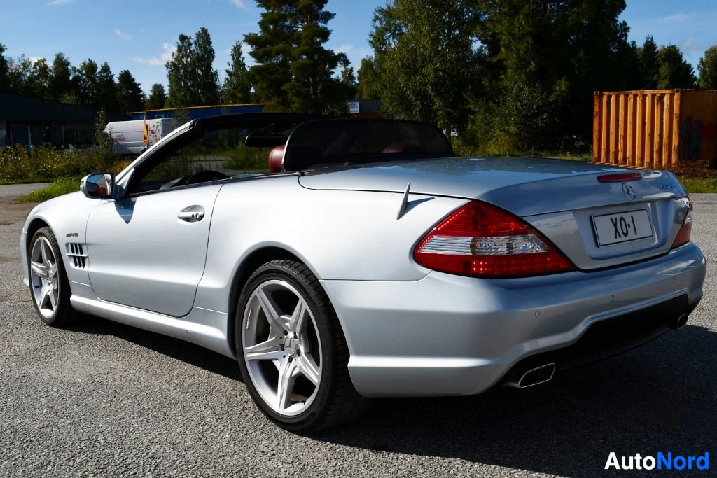 Takaviisto: Mercedes-Benz SL-avokattoauto takaviistöstä, vaalean hopeinen koripinta, punaiset takavalot ja kahdesta putkesta merkitty takapuskuri, rekisterikilpi XO·1.