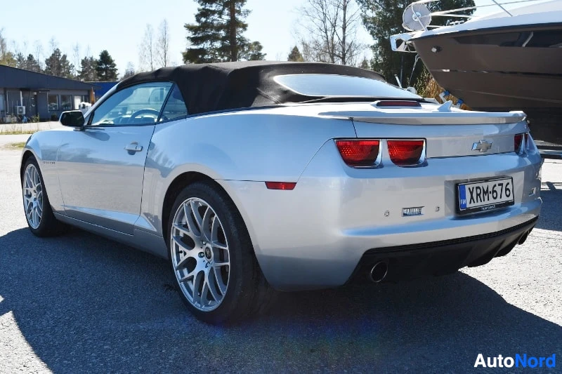 Takaviisto: Hopeanharmaa avokori Chevrolet Camaro takaa oikealta, tumma kangaskatto ylhäällä, rekisteritunnus ja kaksoispakoputket.