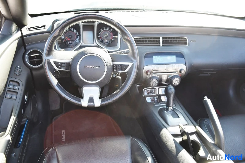Muu: Chevrolet Camaron ohjaamo etupuolelta: ratissa CAMARO-logo, mittarit, automaattivaihteiston valitsin, käsijarru ja keskikonsolin näyttö.