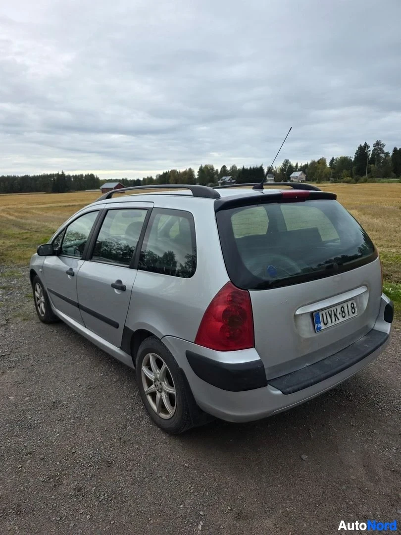 Takaviisto: Hopeanvärinen farmariauto kuvattu takakulmasta oikealta pellon reunassa, rekisterikilpi.