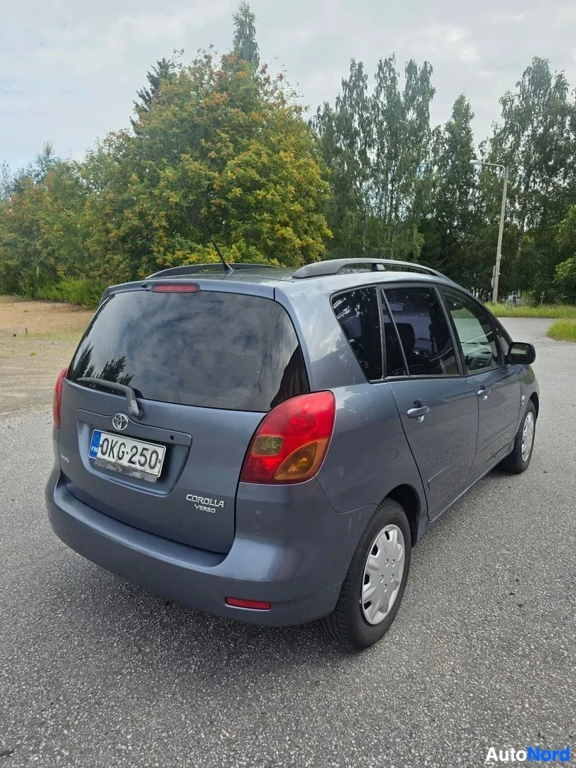 Takaviisto: Sinertävänharmaa tila-auto takaa vasemmalta kuvattuna, rekisteritunnus, kattokaiteet ja Toyota Corolla Verso -teksti takaluukussa.
