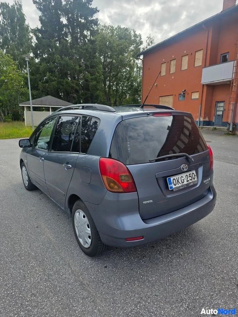 Takaviisto: Sinertävänharmaa tila-auto takaa vasemmalta kuvattuna, rekisteritunnus, kattokaiteet näkyvissä.