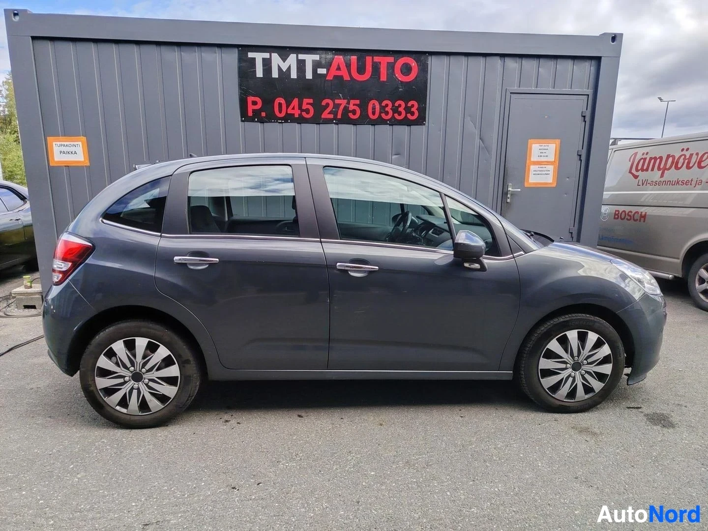 Etuviisto, nokka oikealle: Citroën C3 -viistoperä autopaikan edessä sivusuunnasta, tummanharmaa kori ja hopeanväriset kevytmetallivanteet.