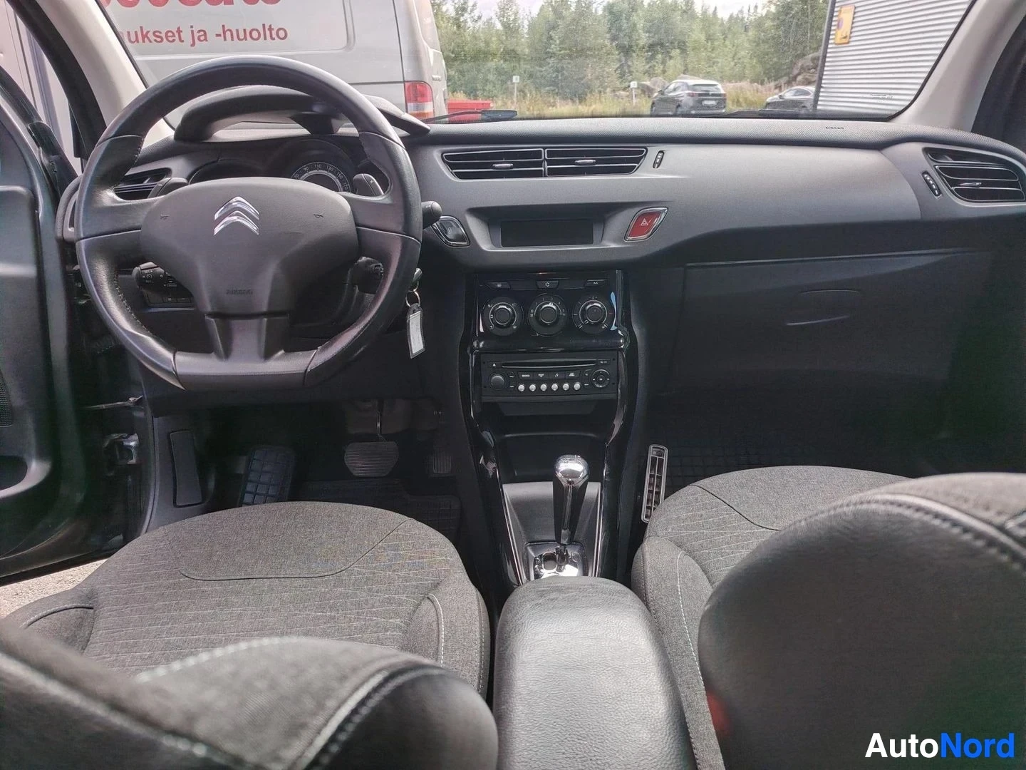 Ohjaamo: Ohjaamo vasemmalta: Citroënin ratin takana kojelauta, keskikonsolissa automaattivaihteen valitsin, radio ja kolme säädinsäädintä.