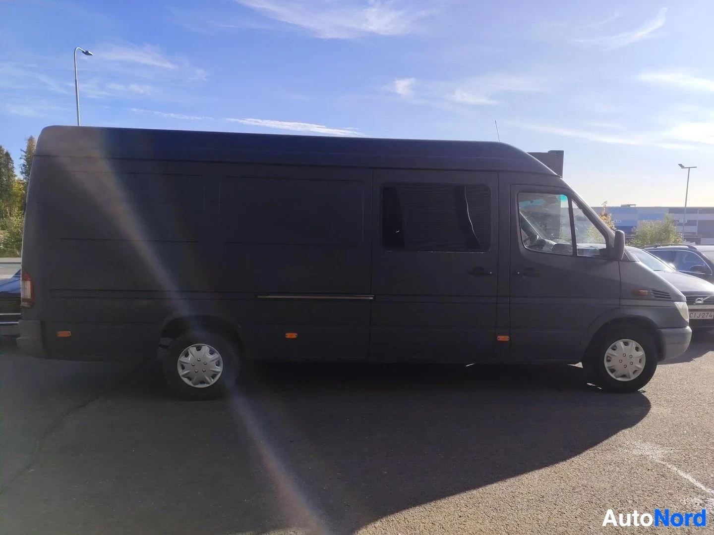 Sivulta: Mercedes-Benz Sprinter -pakettiauto sivulta vasen kylki näkyvissä, tumma kori ja pitkä akseliväli.