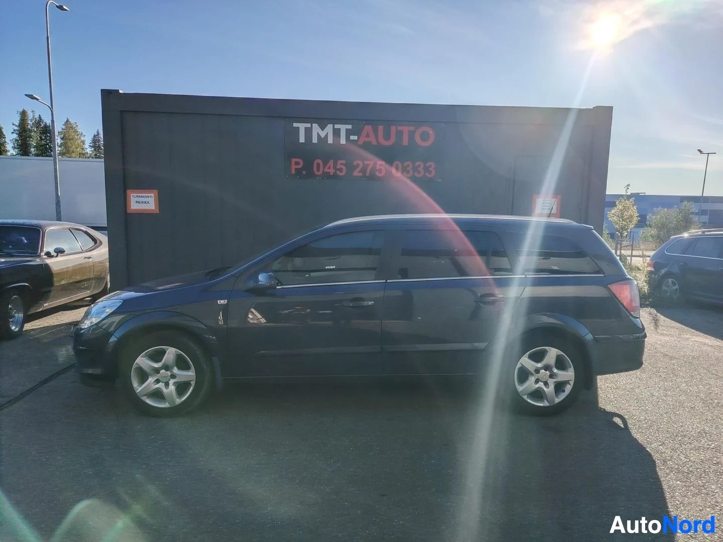 Sivulta: Tummansininen farmariauto sivukuvasta vasemmalta, auringon heijastus kuvassa.