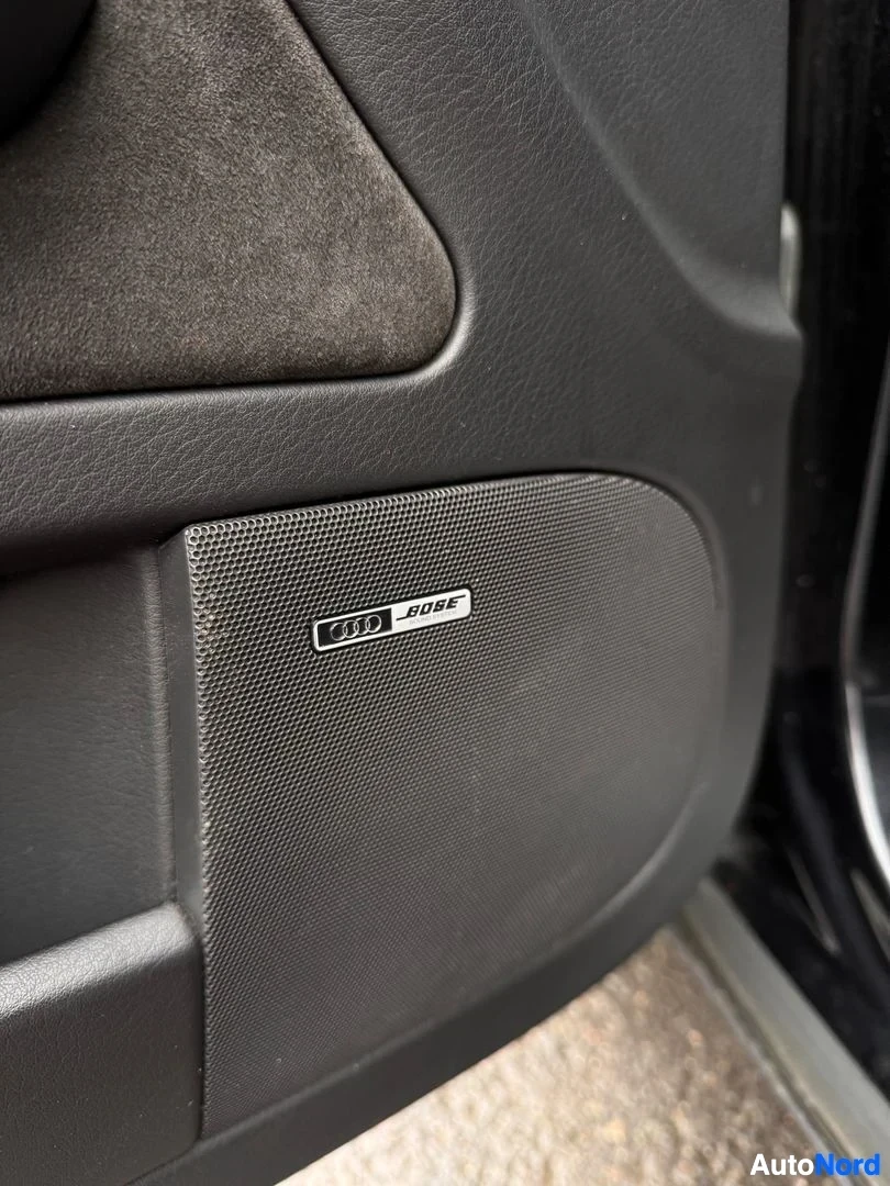 Yksityiskohta: Oven sisäpaneelin kaiutinkangas, jossa Audi- ja Bose-merkinnät.