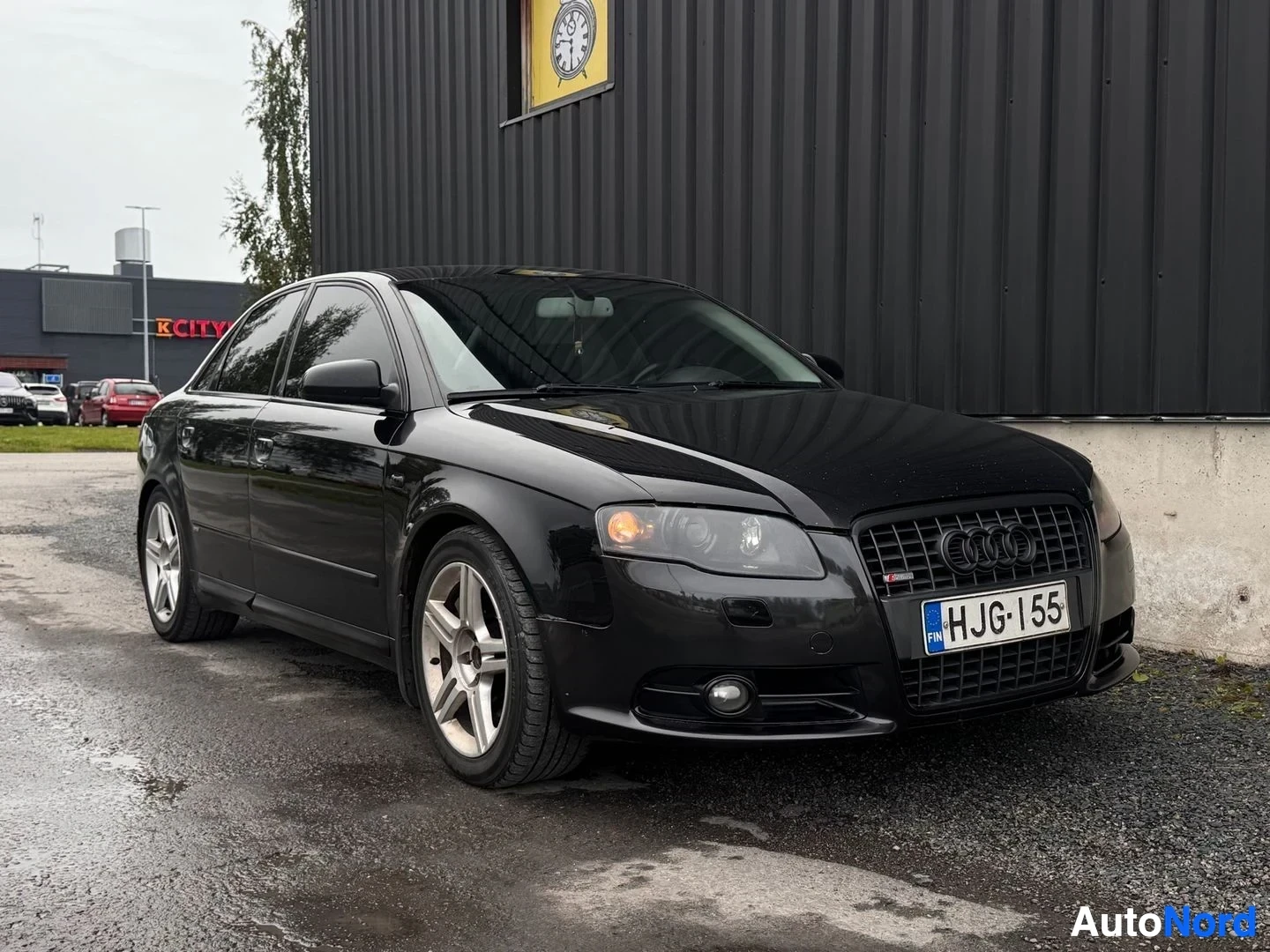Etuviisto, nokka oikealle: Mustan sedanin etukolmasosan kuva oikealta; Audi-ritarit säleikössä, rekisterikilpi.