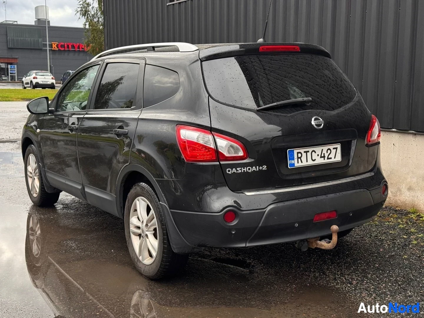 Takaviisto: Mustan Nissan Qashqai+2:n takakulmakuva vasemmalta; takana QASHQAI+2-teksti, rekisterikilpi, takavälipiuhkutin ja kattokaiteet.