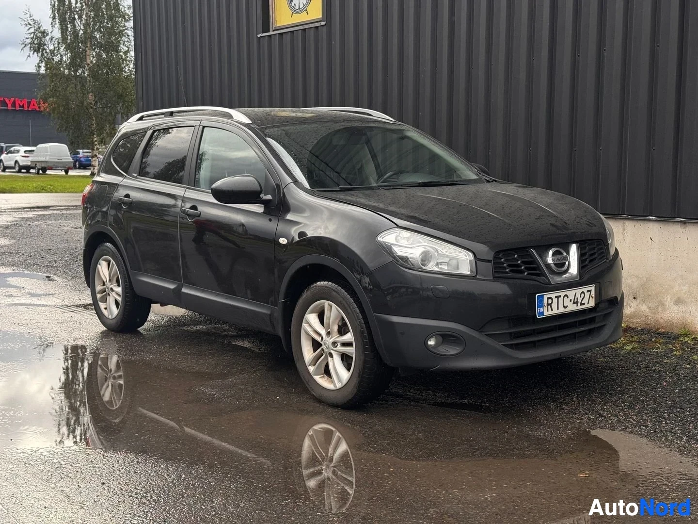 Etuviisto, nokka oikealle: Musta Nissan Qashqai +2 kolmivartalokulmassa edestä oikealta, rekisterikilpi, hopeiset kattokaiteet.