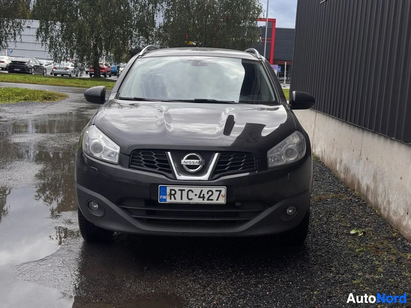 Edestä: Nissan Qashqai +2 suoraan edestä kuvattuna, Nissan-merkki jäähdyttäjän suojassa ja rekisterikilpi.