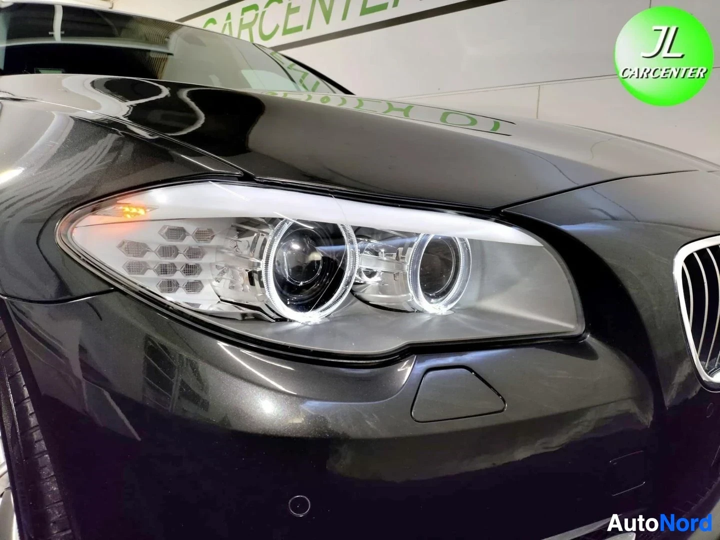 Edestä: BMW 5 Touring -näkymä lähikuvassa: tumma etupänä ja osittain näkyvä etusäleikkö, kuvan painopiste erikoisvalaistussa ajovalossa.
