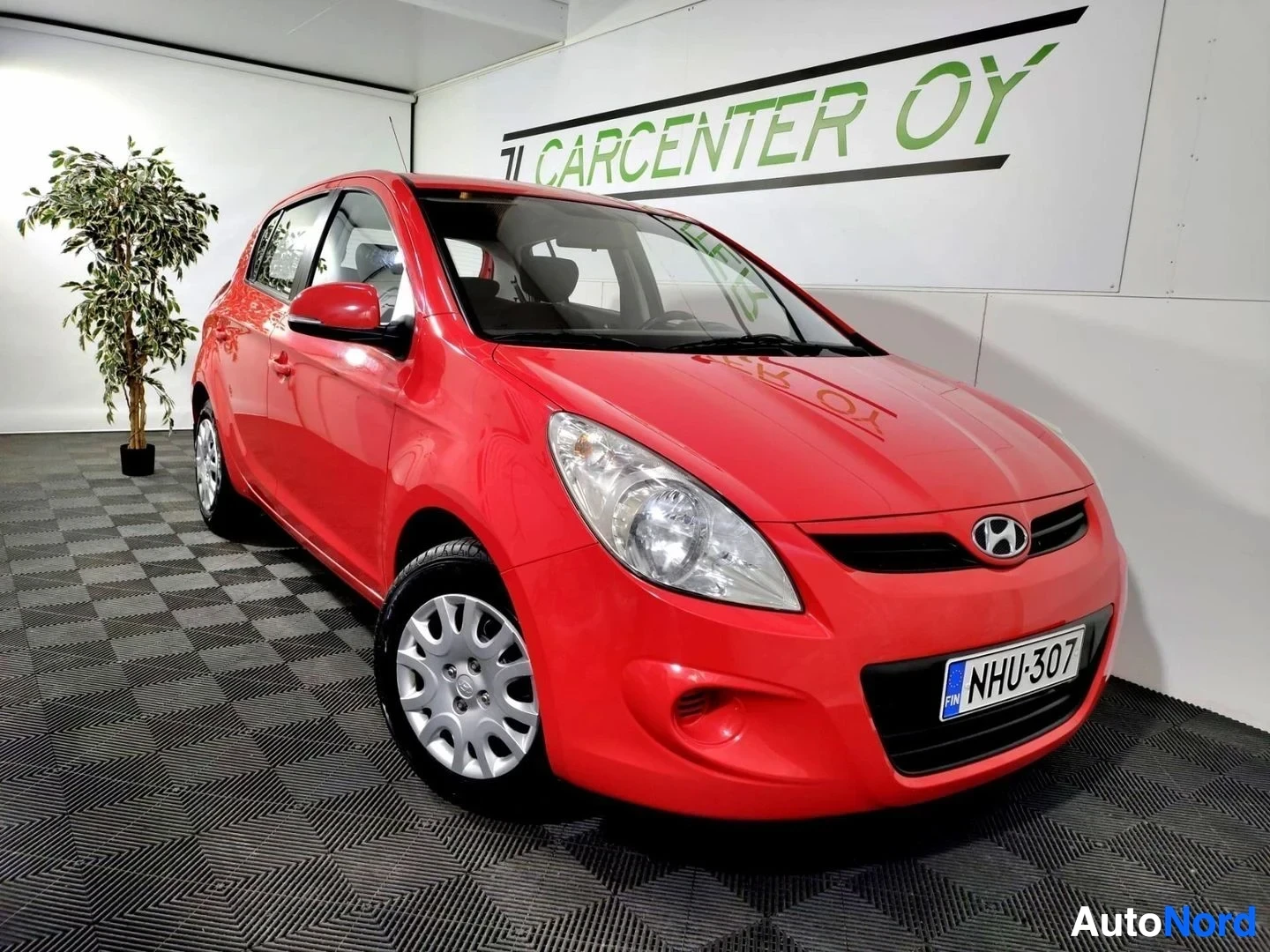 Etuviisto, nokka oikealle: Punaisen Hyundai i20 -henkilöautin etukulman että oikea sivu näkyvät sisätiloissa.