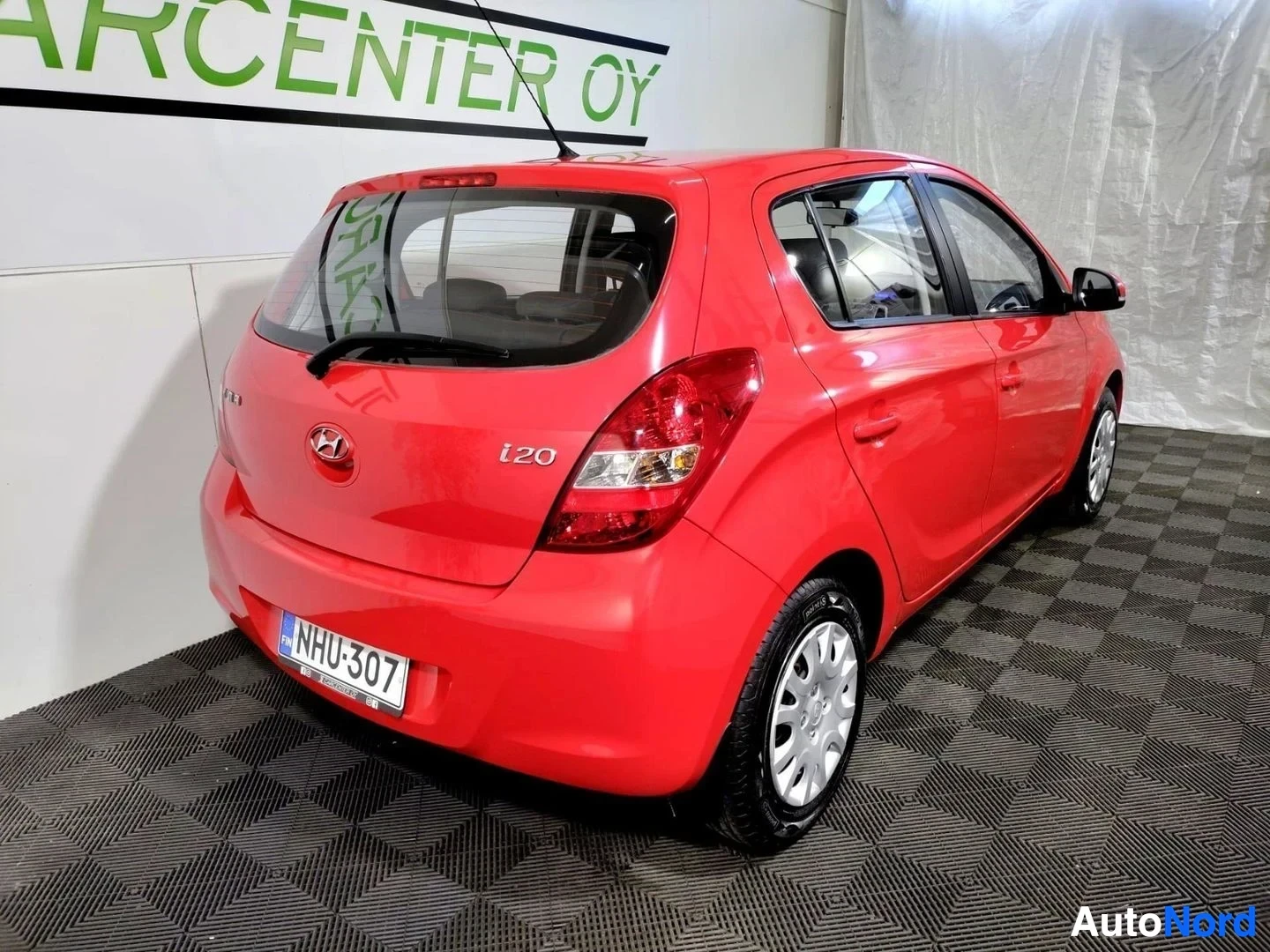 Takaviisto: Punaisen Hyundai i20 -henkilöautin takakulma ja oikea sivu näkyvät sisätiloissa, rekisterikilpi.