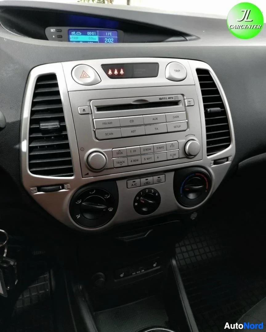Takaa: Keskikonsolin lähikuva: radio (CD, AUX, FM/AM), A/C-nappi ja kolme ilmastoinnin säätörullaa, ylhäällä näyttö.