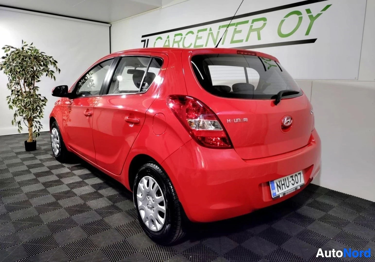 Takaviisto: Punaisen Hyundai i20 -henkilöautin takakulma ja vasen sivu näkyvät sisätiloissa, rekisterikilpi.