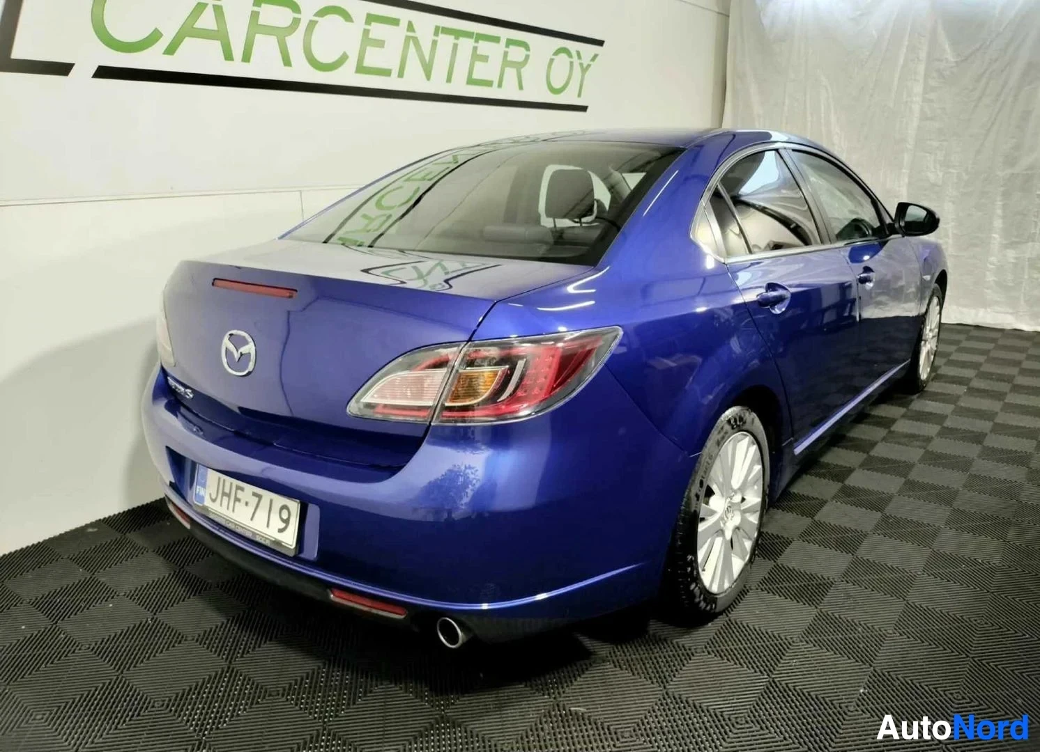Takaviisto: Sininen Mazda 6 -sedan kulmakuva takaa vasemmalta, takavalot ja rekisterikilpi näkyvissä.