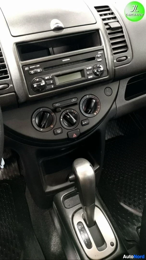 Sivulta: Keskikonsolin lähikuva: Nissan-radiosoitin, kolme ilmastoinnin säätörinkiä ja alaospainikkeineen vaihteenvalitsin.