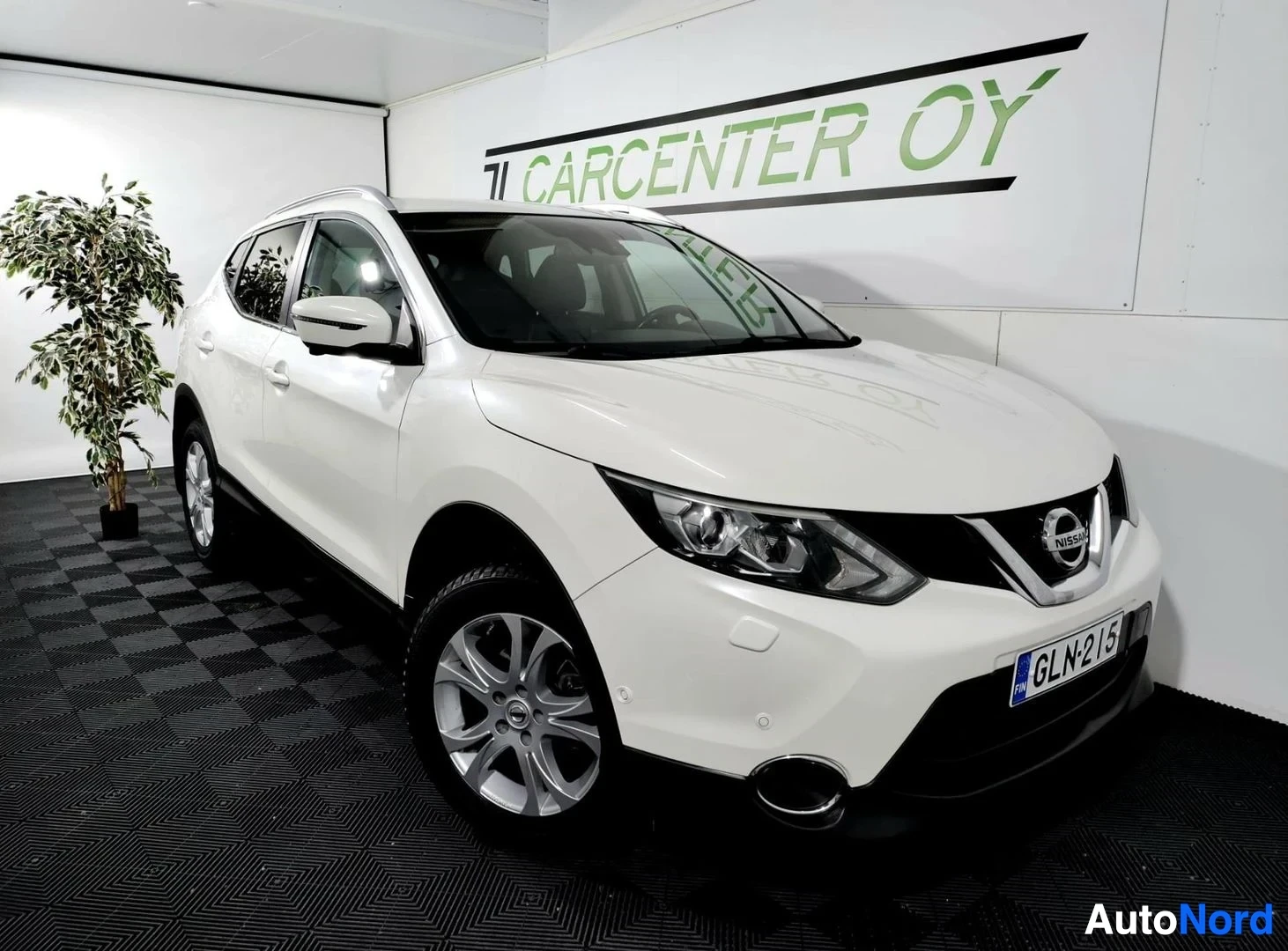 Etuviisto, nokka oikealle: Nissan Qashqai -farmarityylinen auto valkoisena, etukulmakuva oikealta, sisätiloissa.