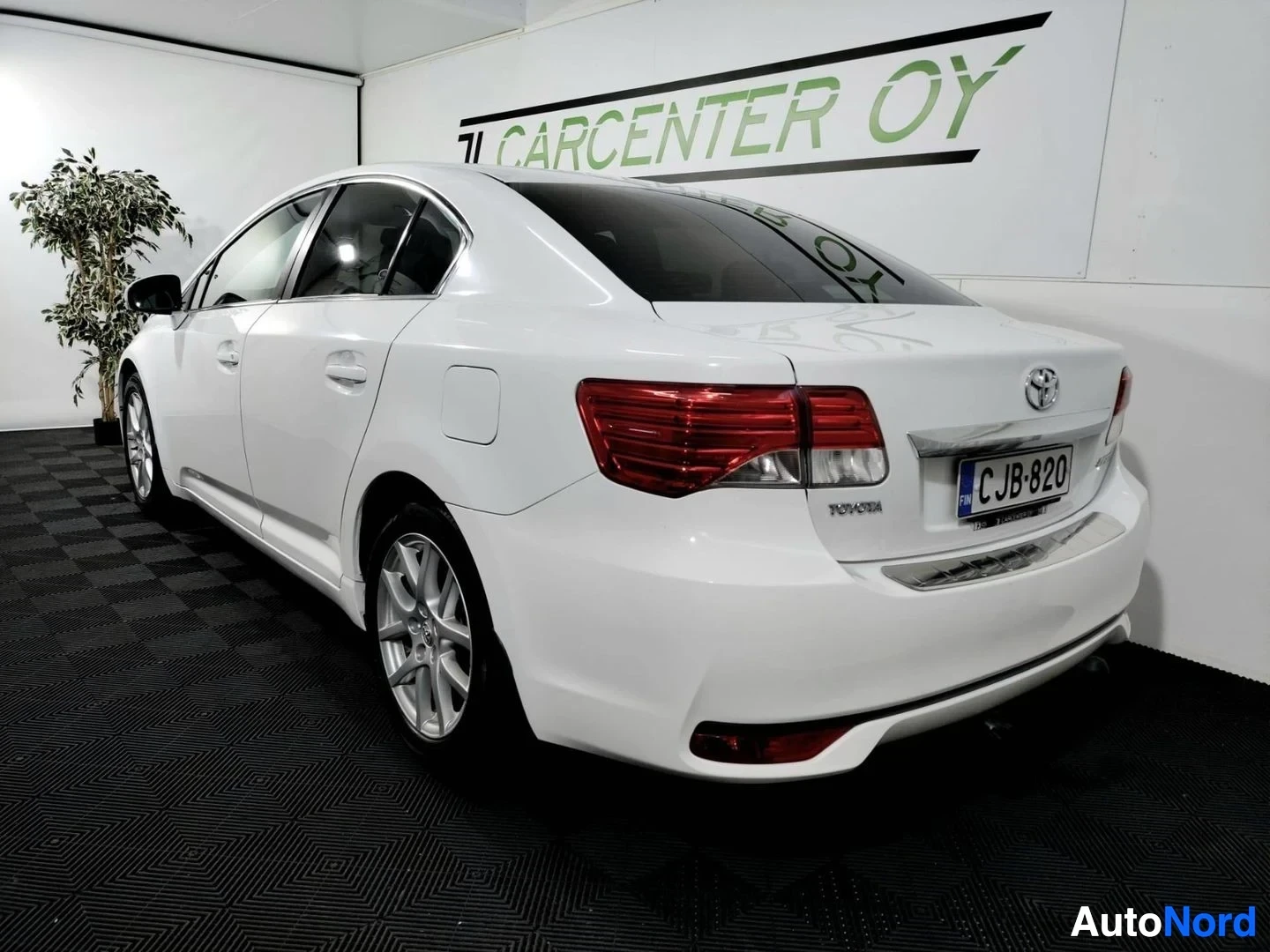 Takaviisto: Toyota Avensisin takapää ja vasen kylki valkoisena, rekisteri, Toyota-merkki takaluukussa.